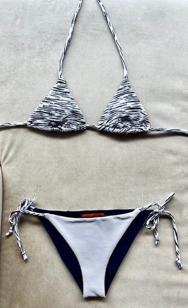 Bikini de cortina de tejido con estructura estampado a rayas blanco y negro. Braguita por delante blanca con tejido de canalé con lurex plata y por detrás del mismo tejido que la parte de arriba.