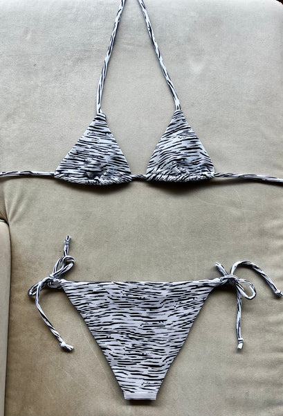 Bikini de cortina de tejido con estructura estampado a rayas blanco y negro. Braguita por delante blanca con tejido de canalé con lurex plata y por detrás del mismo tejido que la parte de arriba.